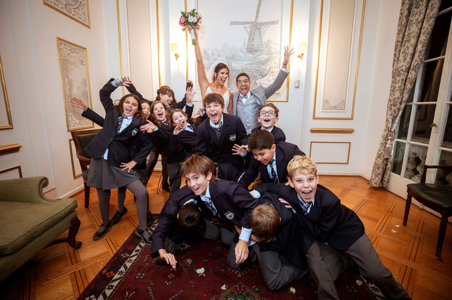 Students in school uniforms celebrate joyfully in an elegant room, jumping and cheering with excitement.