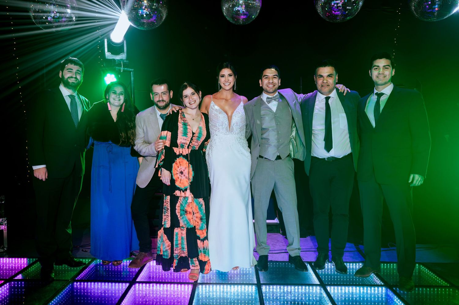 Wedding party poses on illuminated dance floor with disco ball lighting at elegant evening reception.