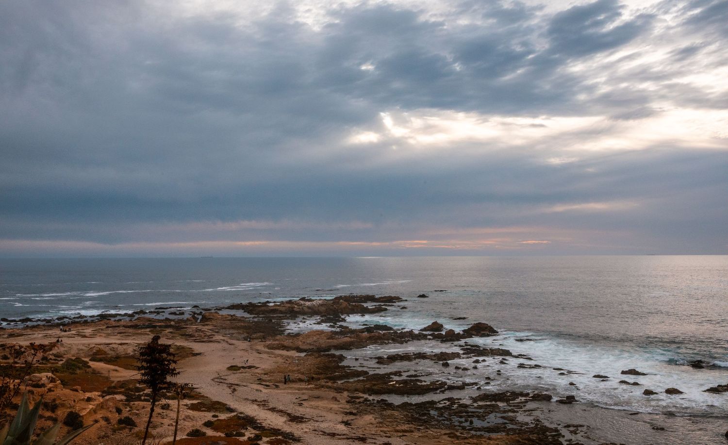Rocky coastal landscape with dramatic cloudy sky at dusk over ocean.
