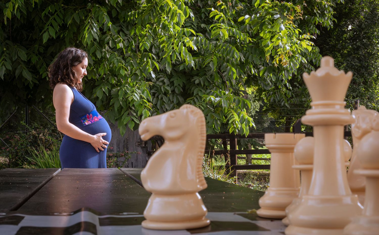 Pregnant woman in navy dress admiring giant chess pieces outdoors.
