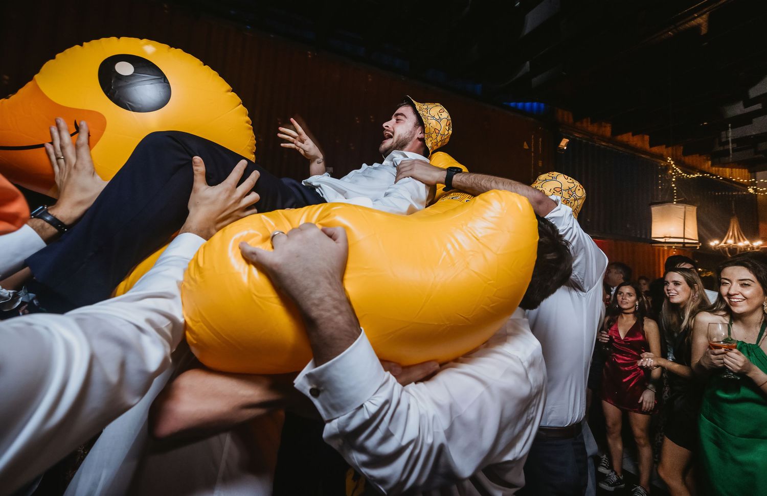 Man crowd surfing on giant inflatable yellow duck at lively party event.