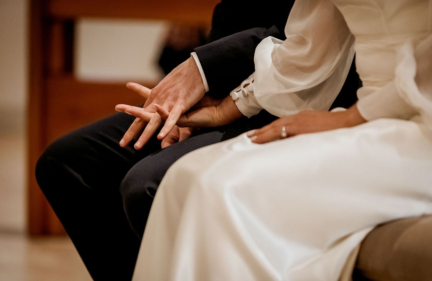 Bride and groom sitting together, hands intertwined, showcasing wedding rings on their special day.