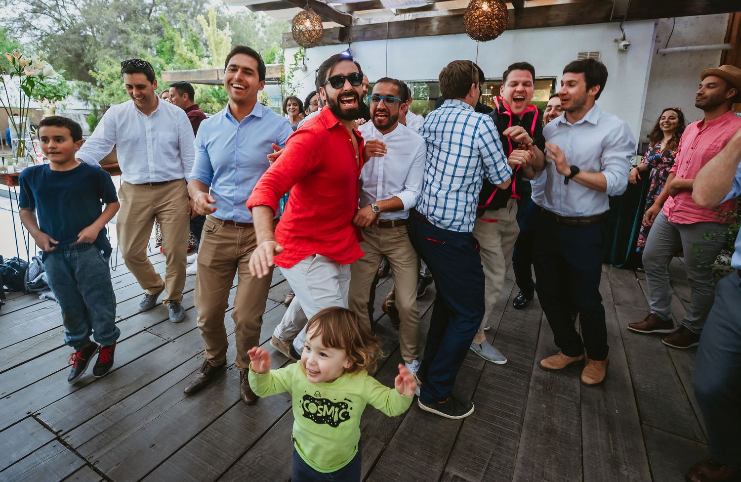 Men and a toddler dancing joyfully at an outdoor party celebration.