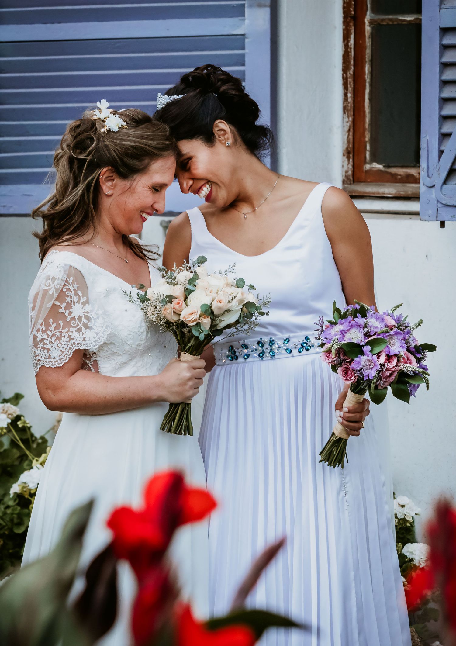 Two brides in white dresses share an intimate moment holding bouquets on their wedding day.