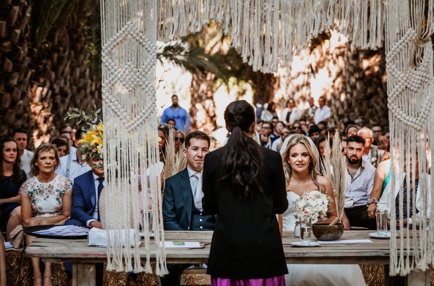 Bride and groom at altar with macrame backdrop during outdoor boho wedding ceremony.