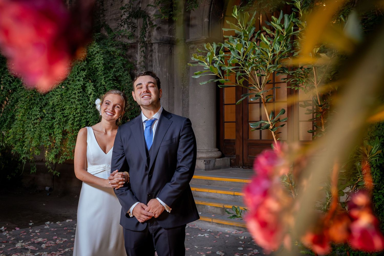 Elegant bride and groom pose together among colorful blooms at outdoor wedding venue.