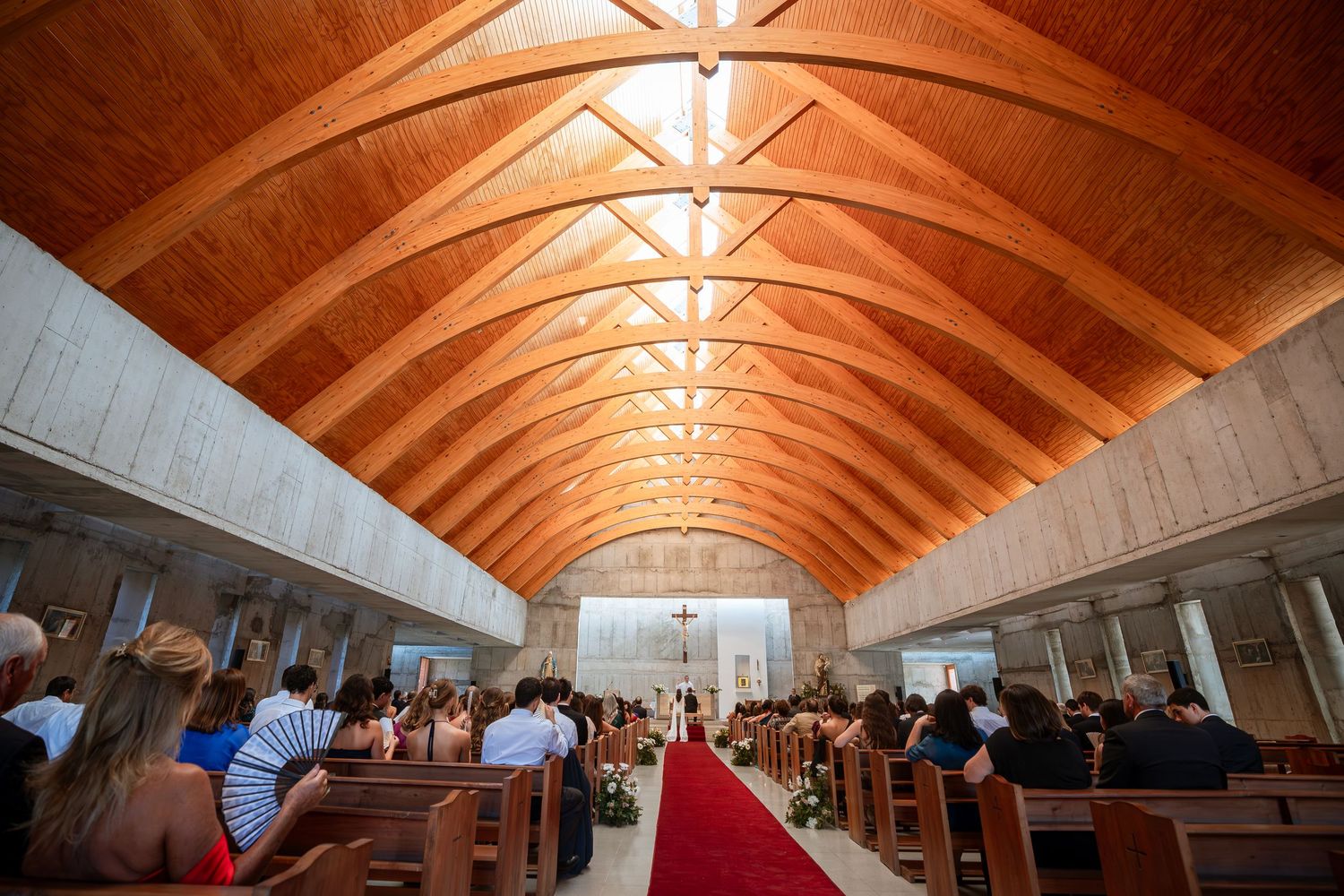 Interior of church with wooden arched ceiling and guests seated for wedding ceremony.
