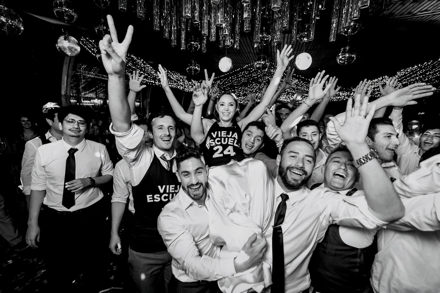 Black and white photo of groom and groomsmen celebrating joyfully at a wedding reception.