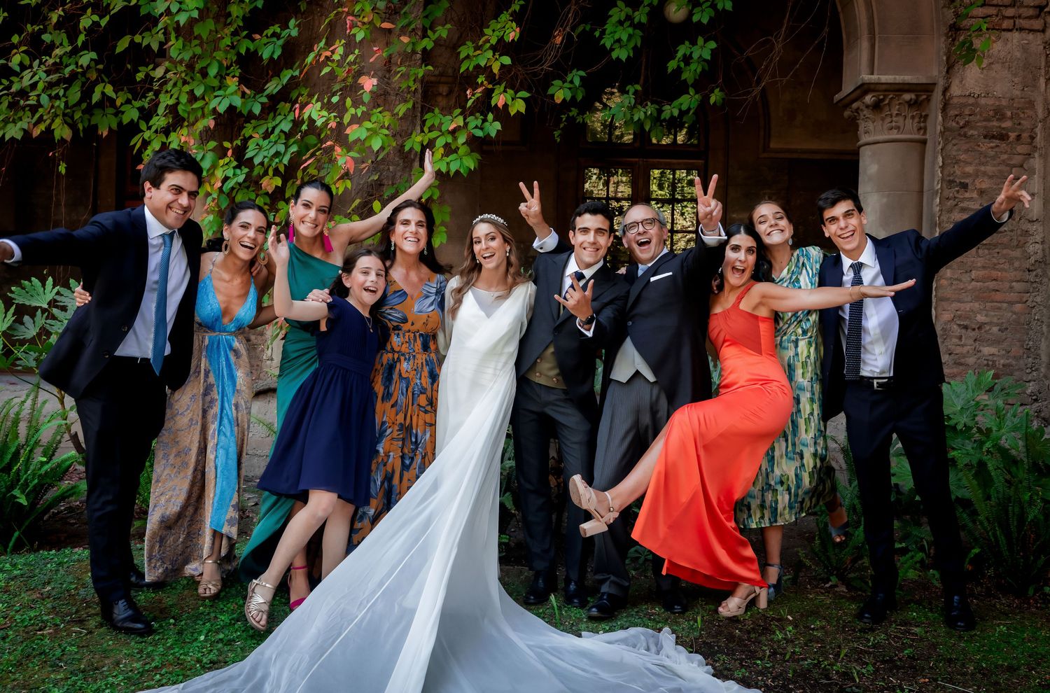 Joyful wedding group photo with bride in white gown and guests celebrating outdoors in a lush garden.
