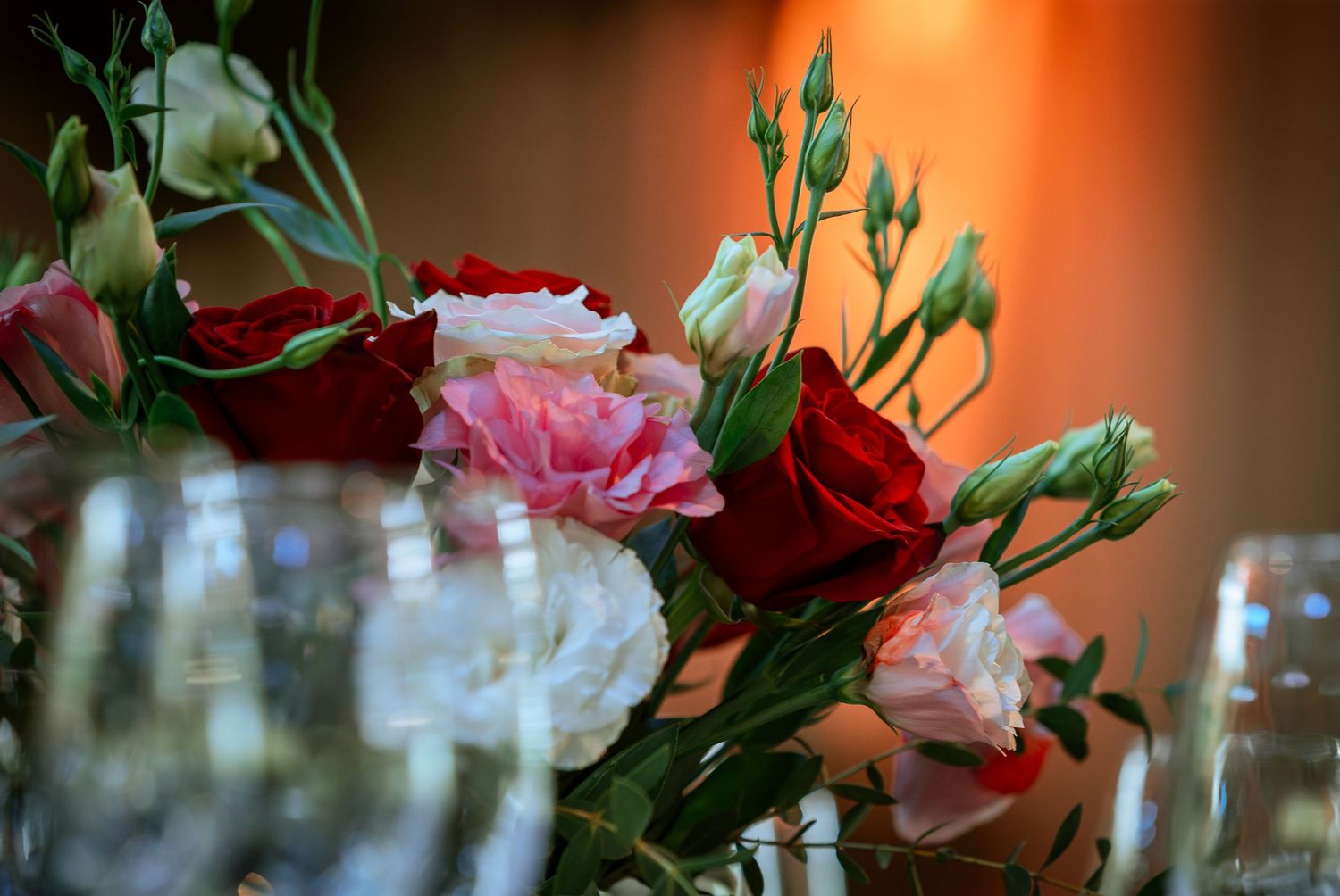 Beautiful wedding centerpiece featuring red, pink, and white roses with greenery beside crystal glasses.