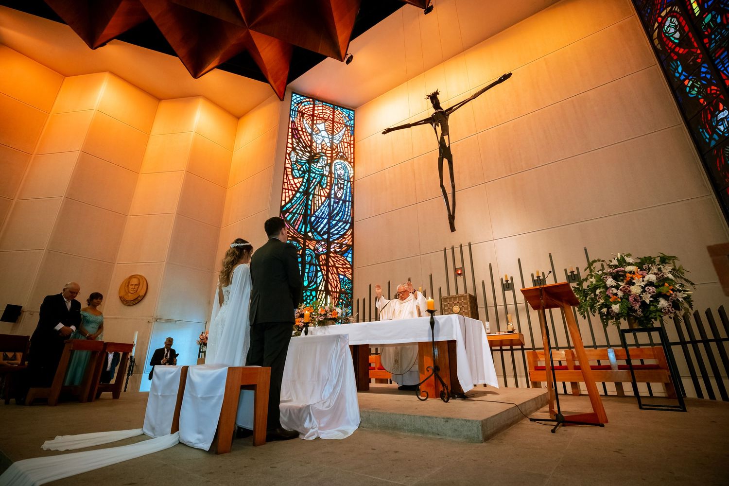 Bride and groom exchange vows at a Catholic church altar with stained glass windows and a crucifix.