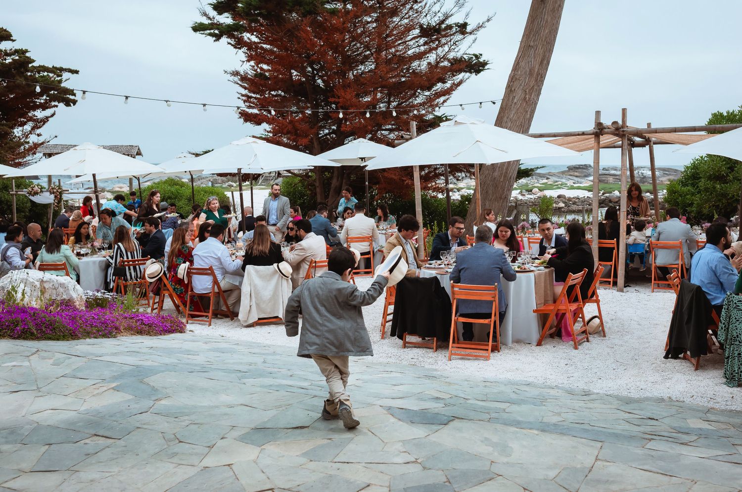 Guests enjoy an outdoor wedding reception dinner under string lights and white umbrellas on a stone patio.