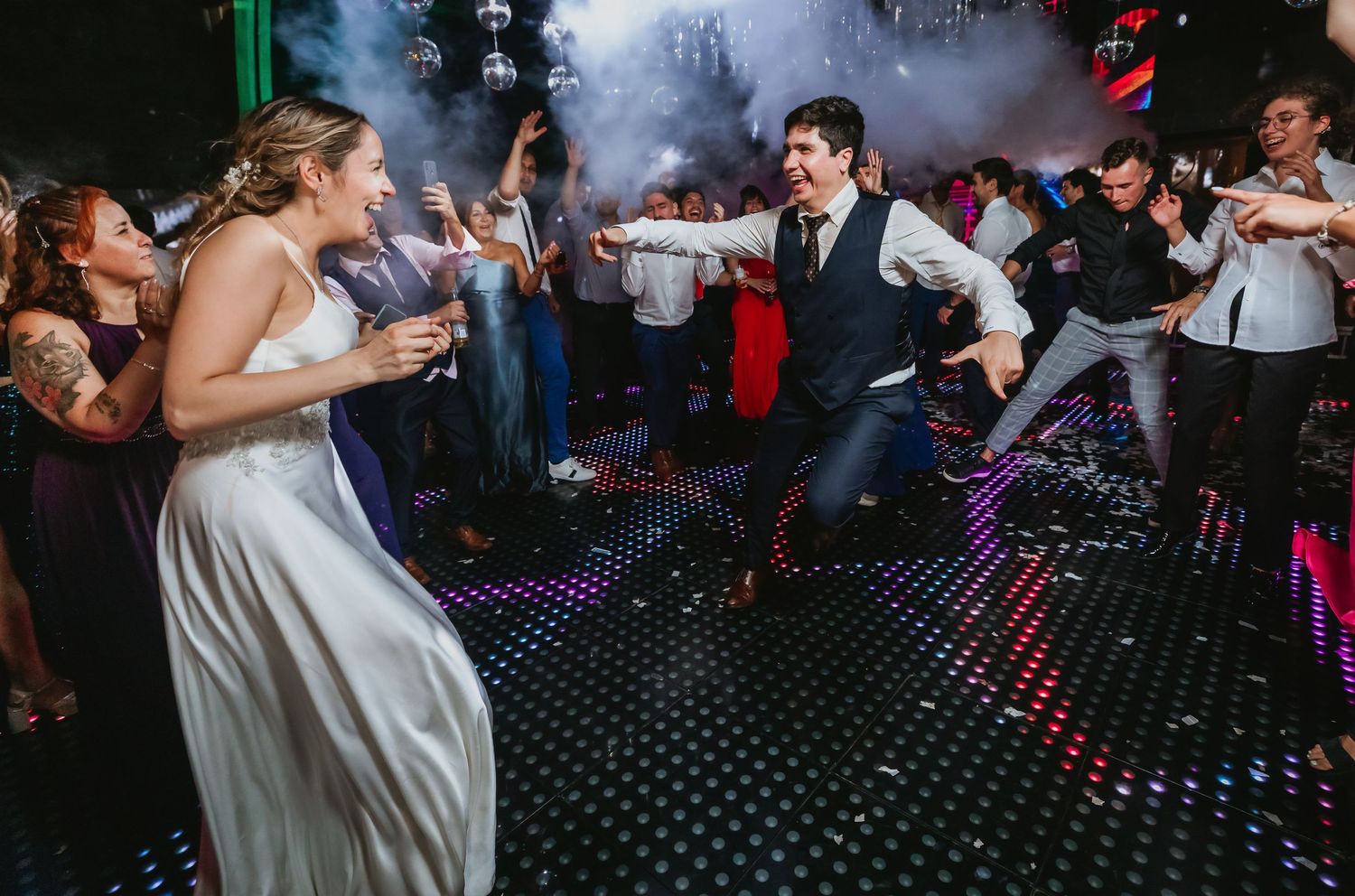 Bride and groom dancing energetically in fog effects on a glittering wedding dance floor.