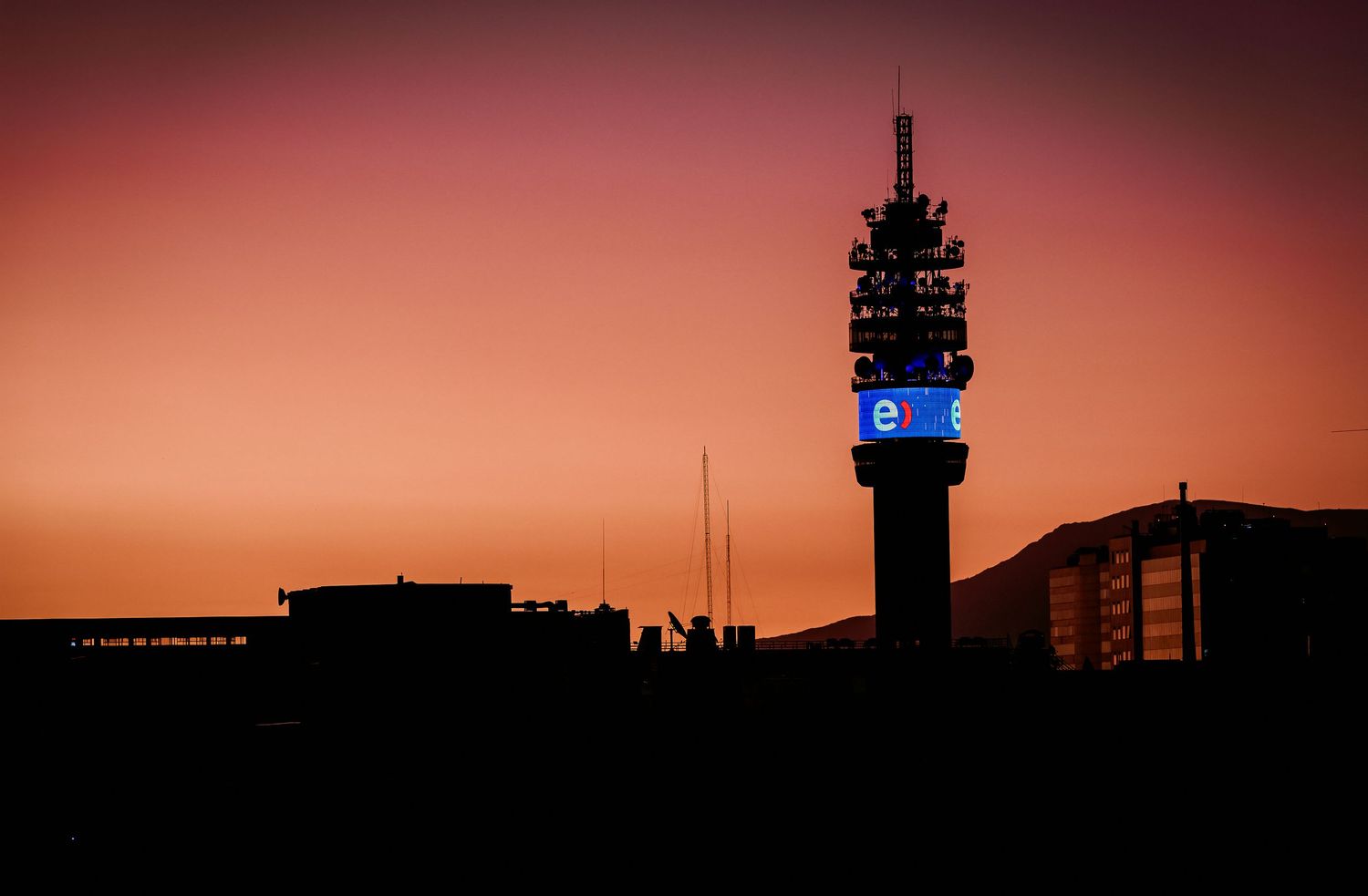Telecommunications tower silhouetted against a vibrant orange and red sunset sky.