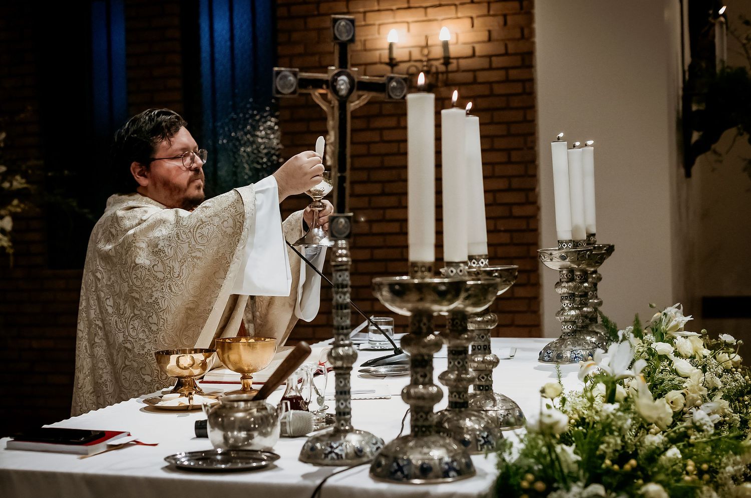 Priest in golden vestments lighting candles on an ornate altar with a crucifix during a Catholic Mass ceremony.