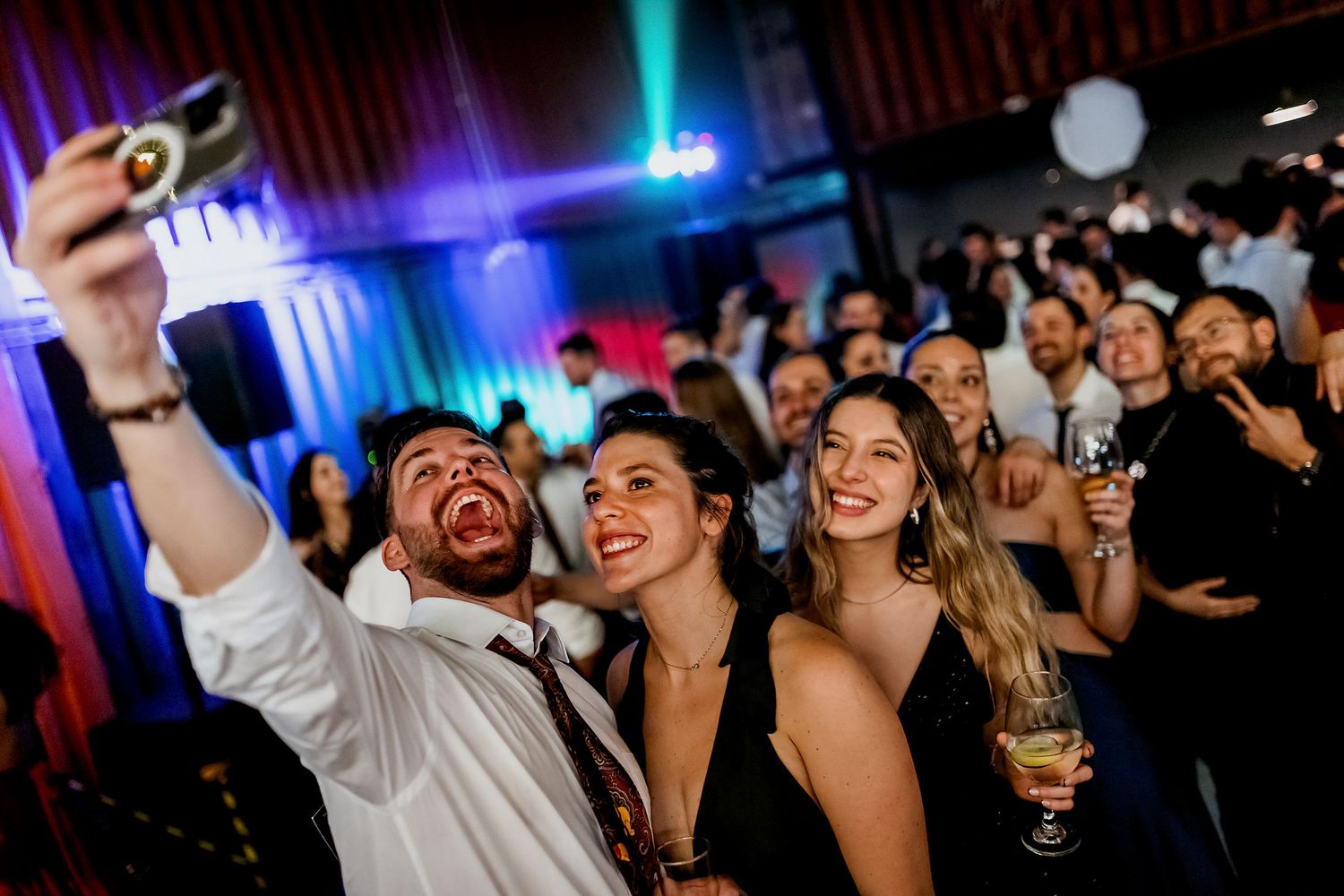 Group of friends taking a selfie at a lively nightclub party with colorful lights in the background.