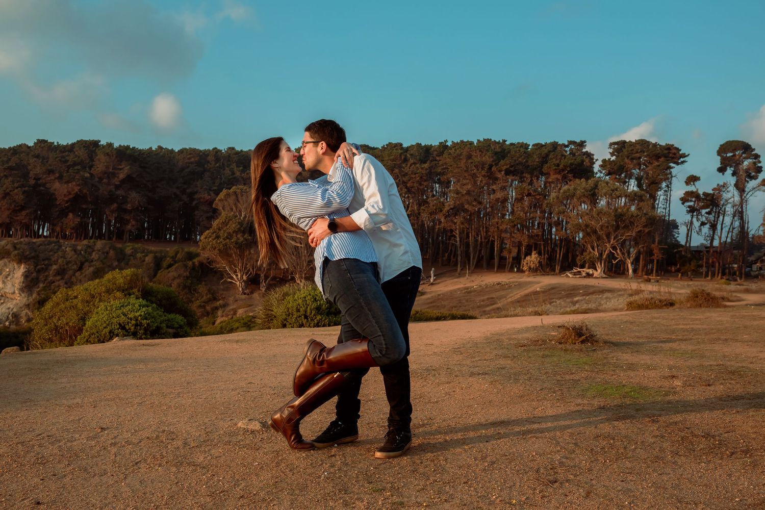 Romantic couple sharing a kiss outdoors on a sunny coastal landscape.