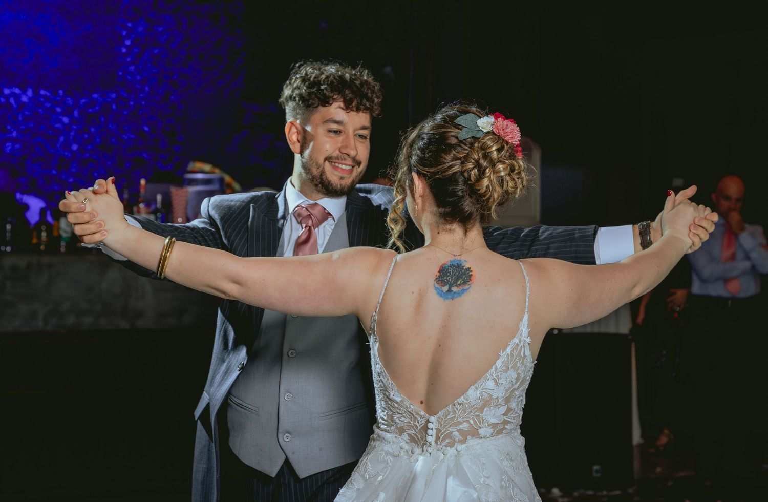Bride and groom share their first dance, with bride's floral back tattoo visible in her backless wedding gown.