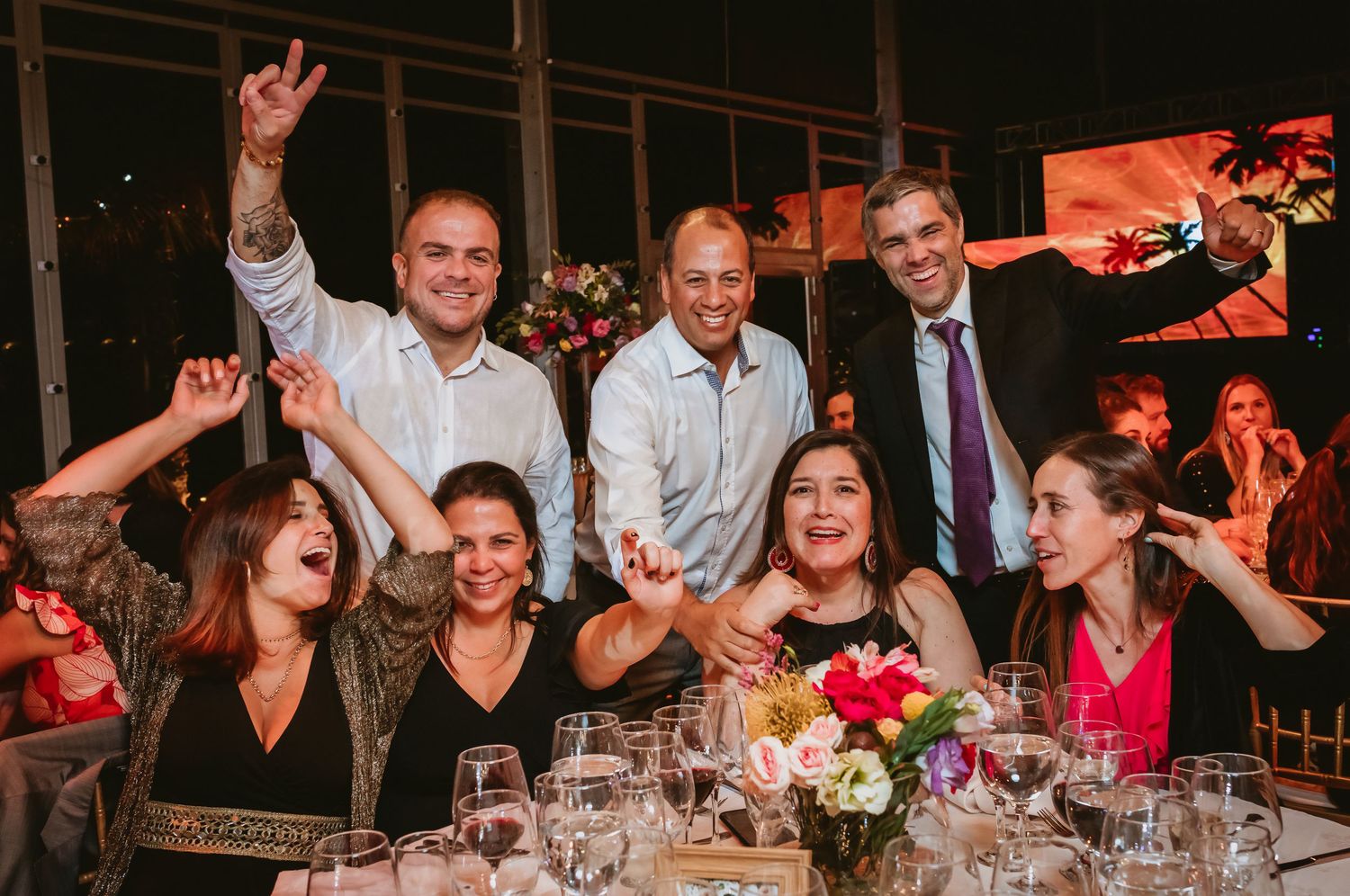 Joyful wedding guests celebrating and posing together at festive reception dinner table.