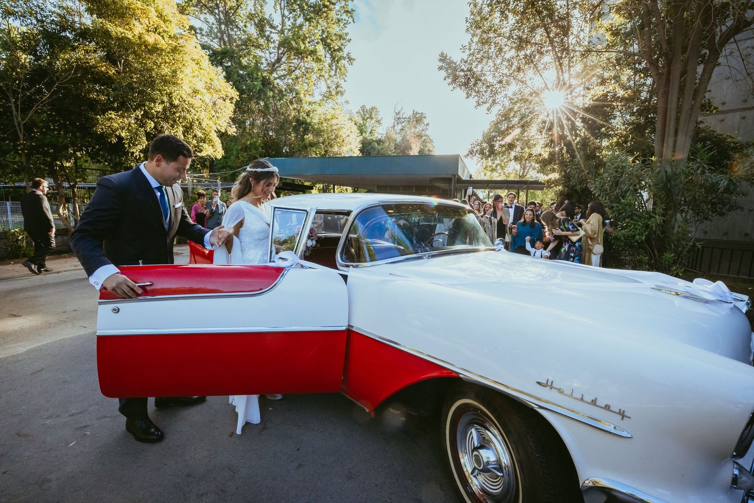 Bride and groom prepare to depart in a classic red and white vintage convertible after their wedding.
