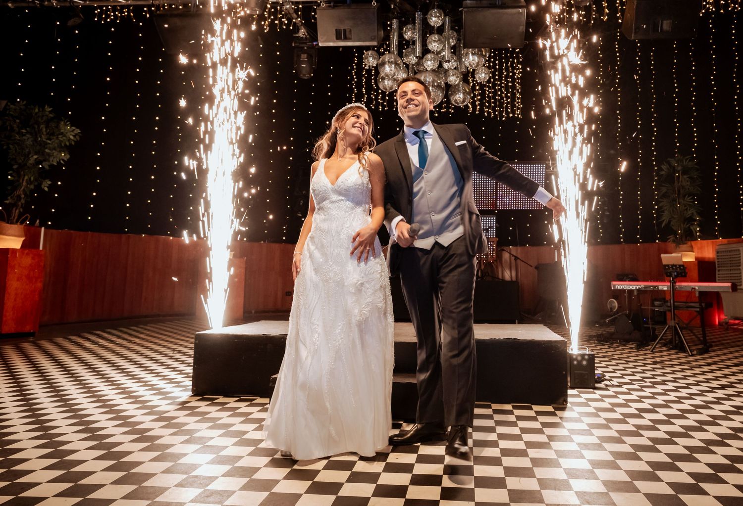 Bride and groom standing on a checkered dance floor surrounded by sparkling wedding fireworks.