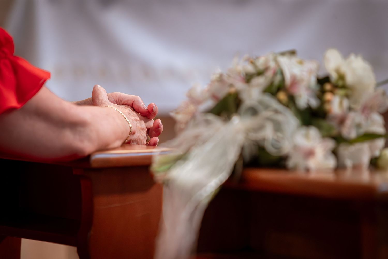 Close-up of folded hands with henna resting on pew beside bridal bouquet during wedding ceremony.