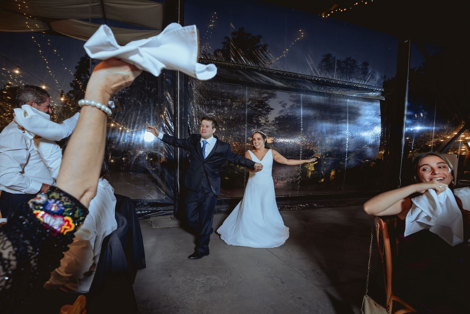 Bride and groom enter wedding reception as guests wave white napkins in celebration.