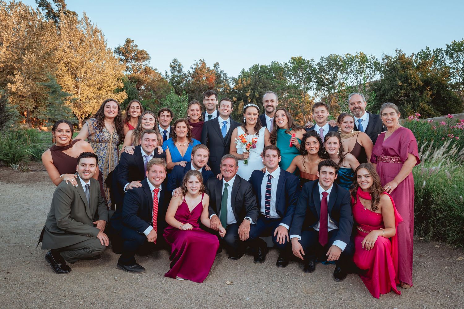Large formal wedding party group portrait outdoors with bride and groom at center.