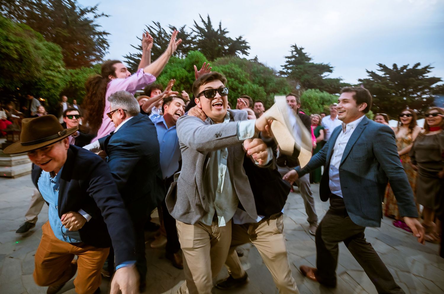 Energetic crowd of wedding guests rushing forward at an outdoor celebration in casual formal attire.