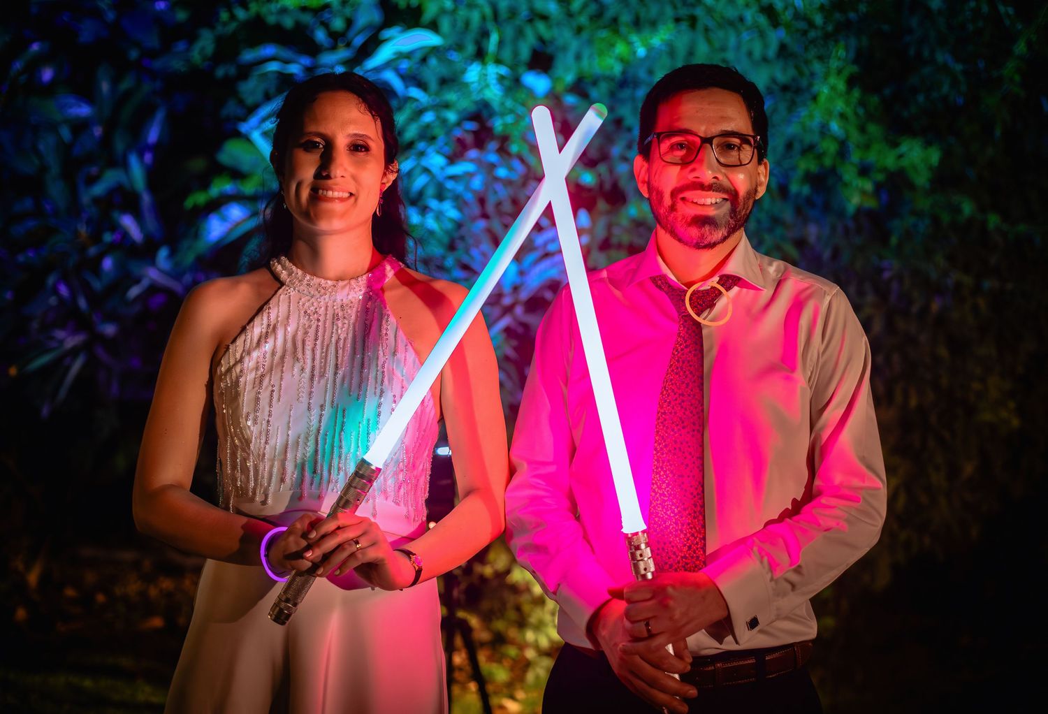 Couple smiles holding crossed blue and pink lightsabers at a Star Wars themed wedding.