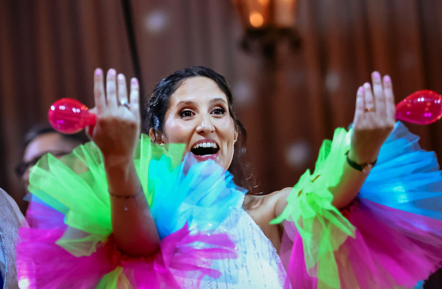 Joyful woman in white dress dances with colorful neon tulle fans at a vibrant party celebration.