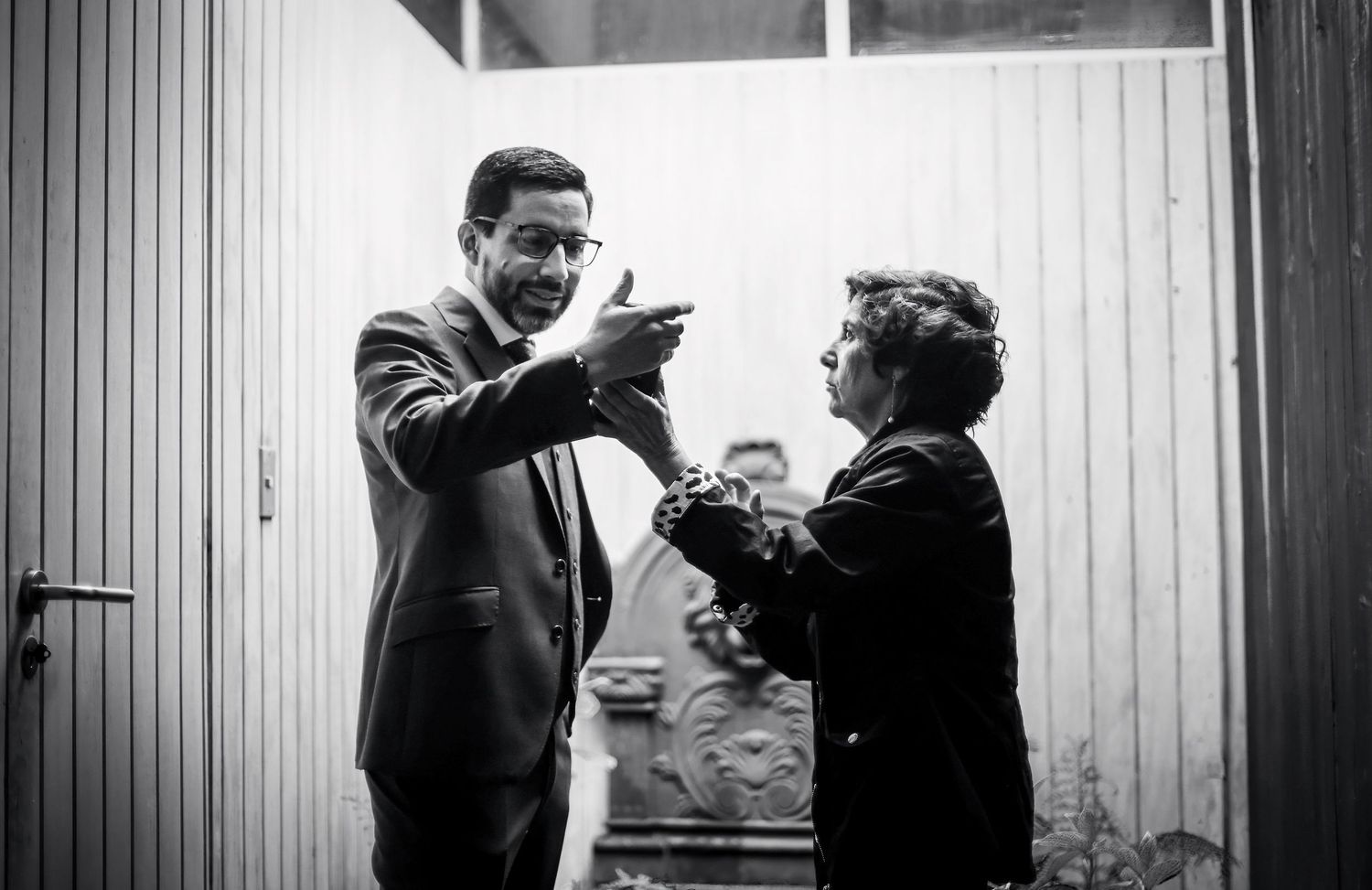 Man in suit gesturing expressively while talking to woman in black and white candid photo.
