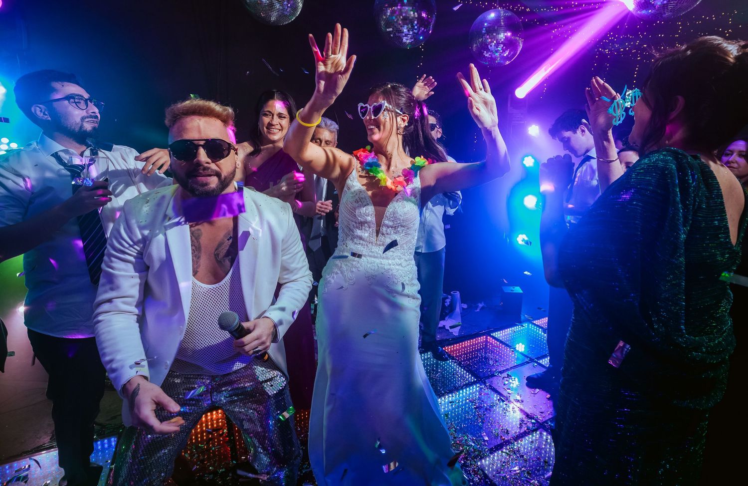 Guests dancing at a vibrant wedding reception with disco lights, confetti, and colorful decorations.