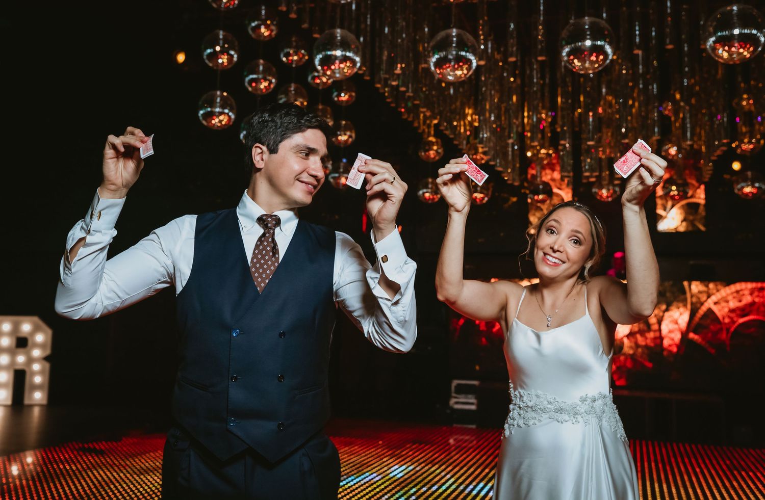 Bride and magician celebrating on stage holding playing cards at a glamorous wedding reception.