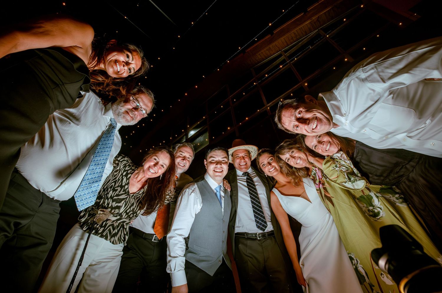 Wedding party forms joyful circle looking down at camera from above at reception.