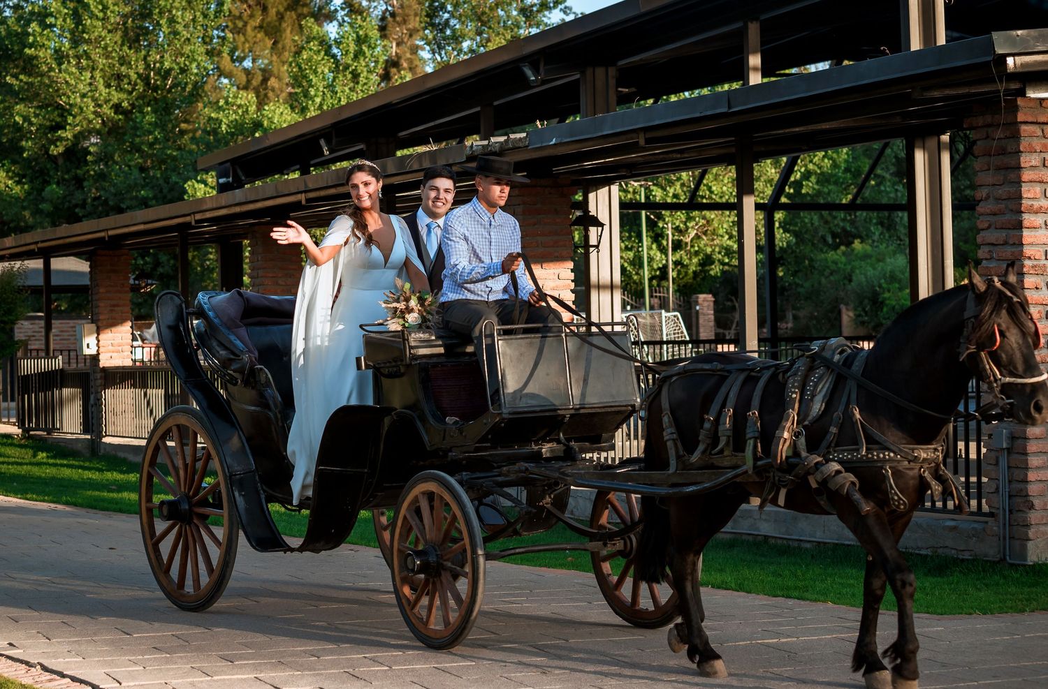 Bride and groom arrive in style riding a classic black horse-drawn carriage at wedding venue.