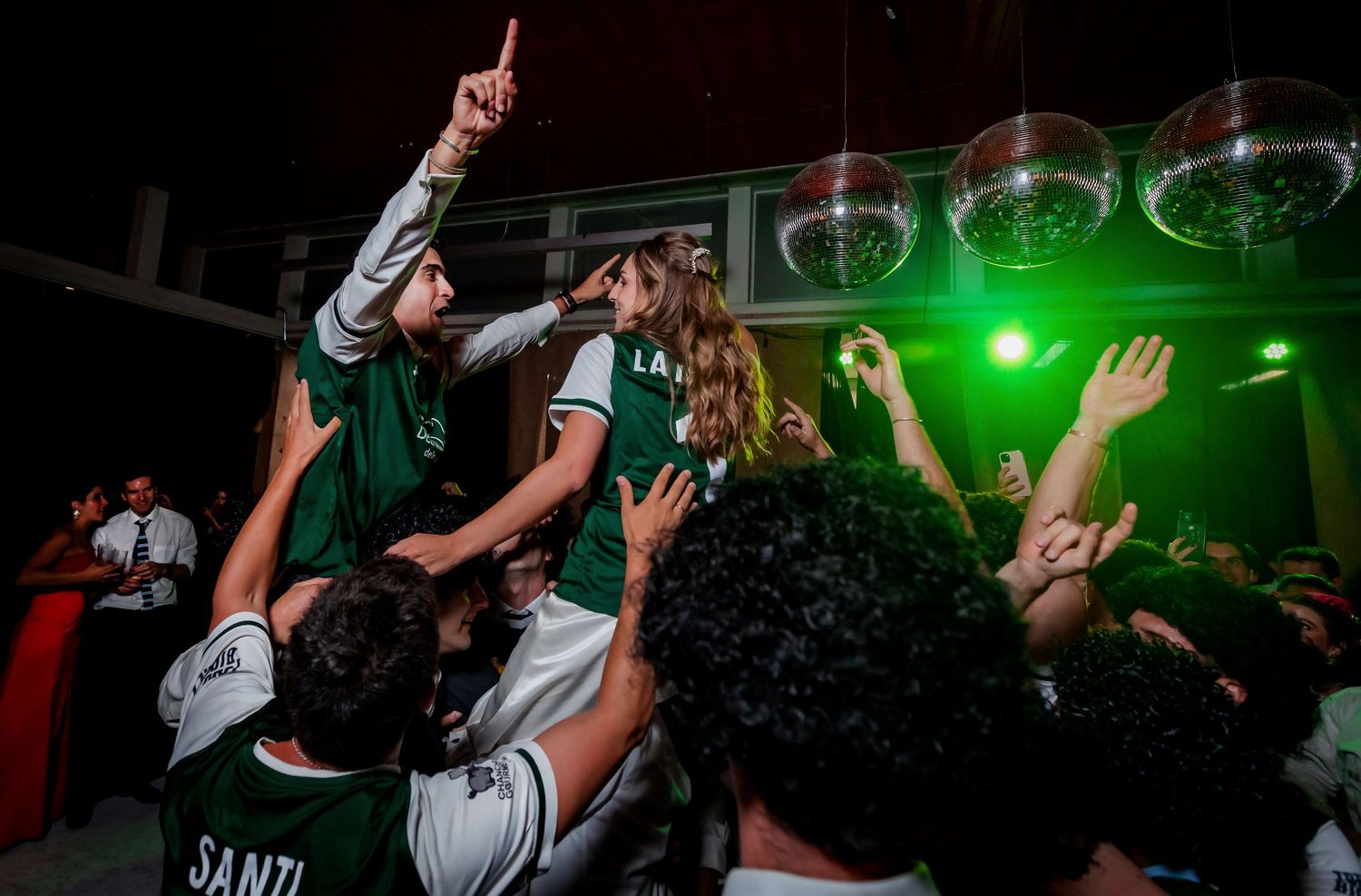 Joyful wedding guests in green jerseys crowd-surf and cheer during an energetic wedding reception party.