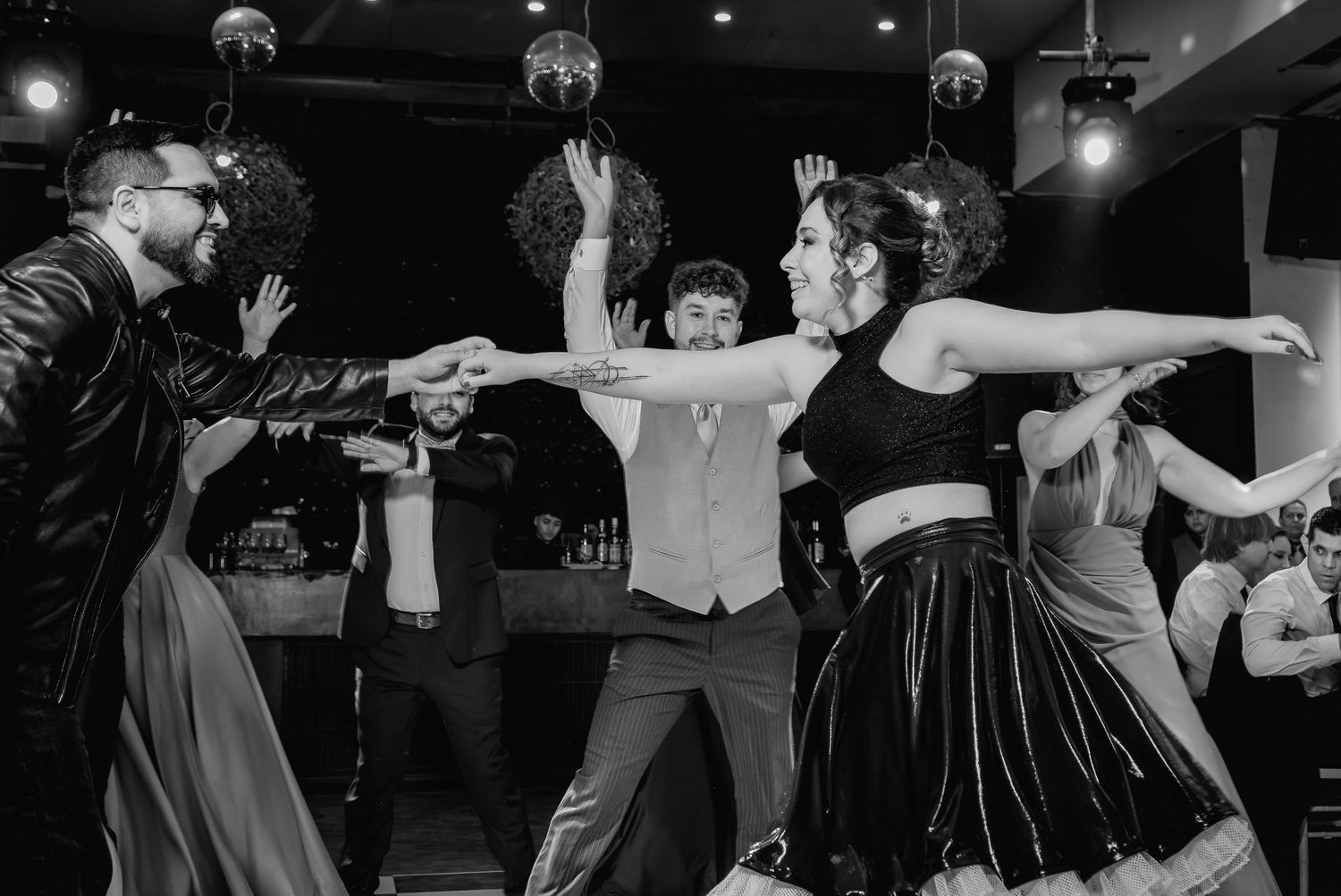 Group of dancers perform lively routine at wedding reception in black and white photography.