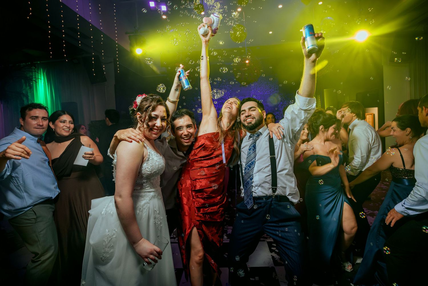 Bride, groom, and friends celebrating with confetti and drinks at wedding reception.