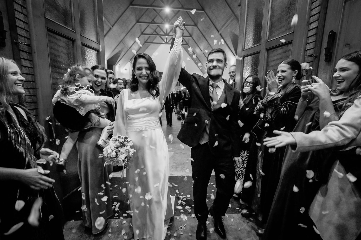 Black and white photo of newlyweds celebrating with confetti as guests cheer outside a church.