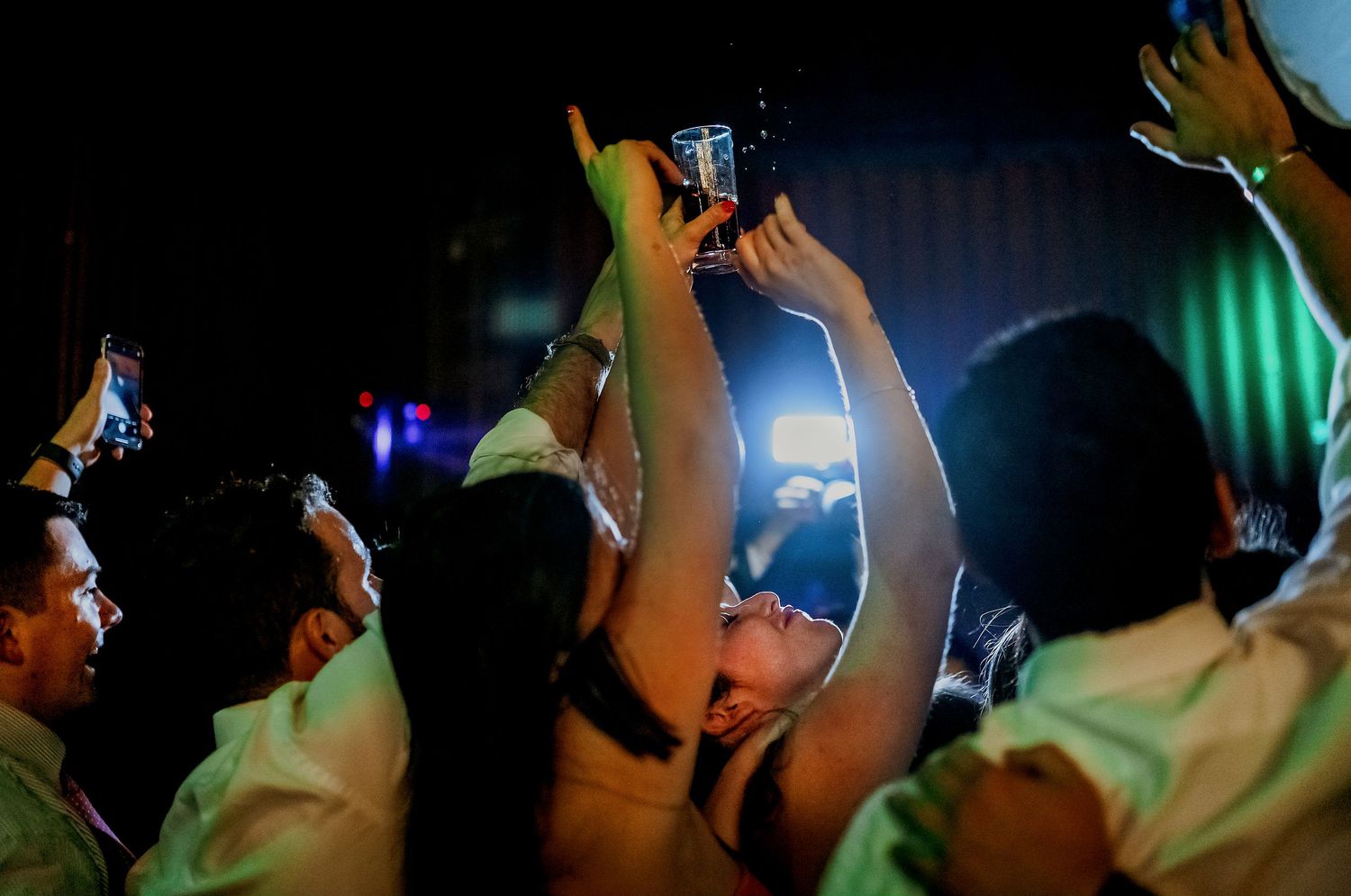Crowd at a concert with a woman holding up a smartphone to capture the moment at a lively nighttime event.