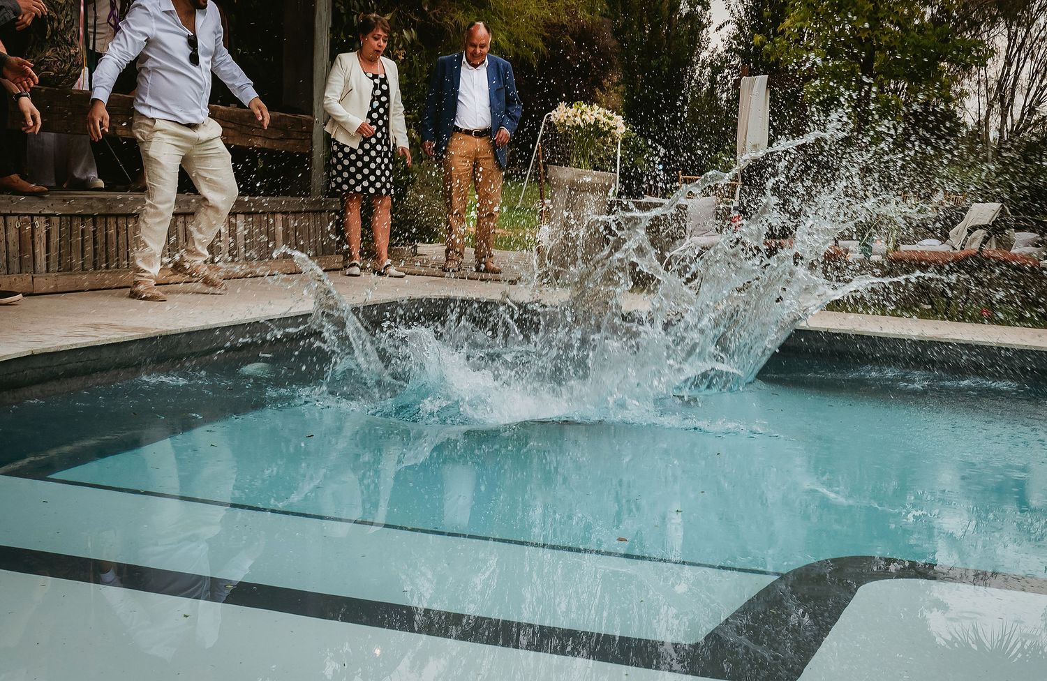 People watching a large water splash in a swimming pool at an outdoor garden party event.