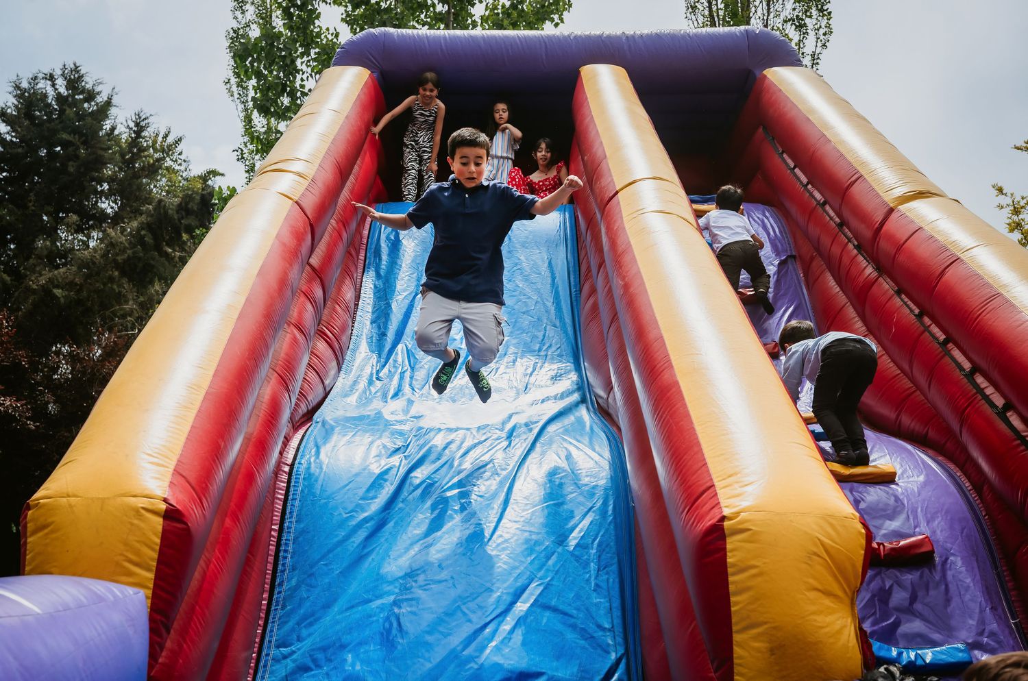A child joyfully jumps on a colorful inflatable slide at an outdoor party event.
