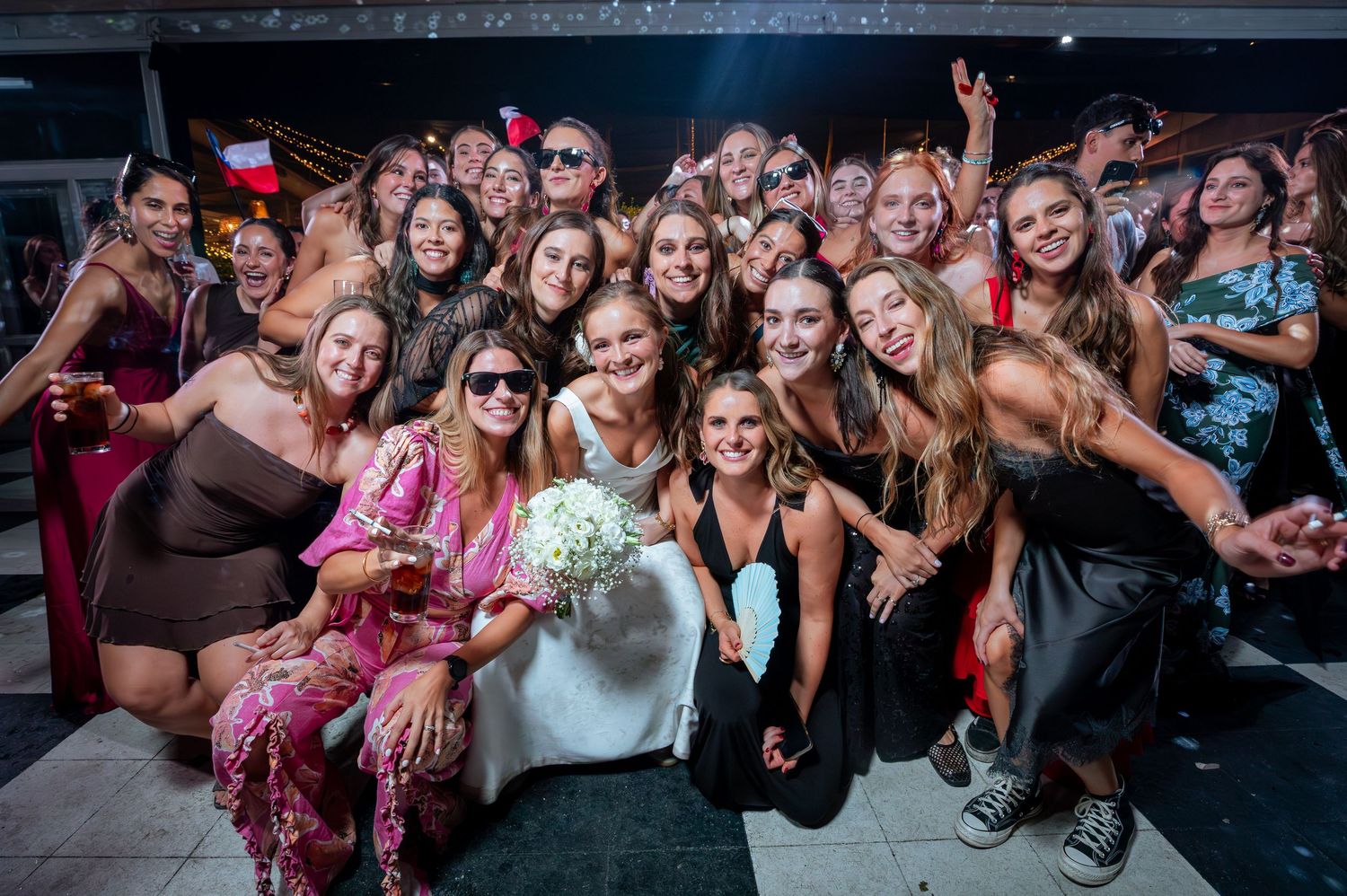 Bride poses with large group of women friends at wedding reception celebration party.