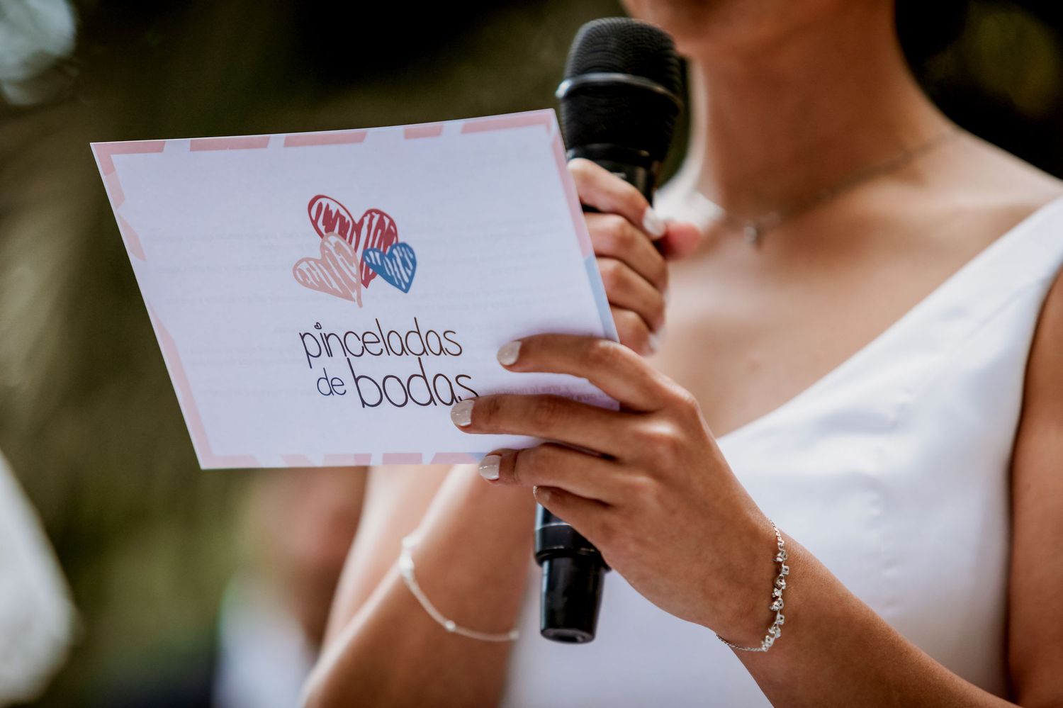 Wedding officiant holds a Pinceladas de Bodas card while speaking into a microphone.