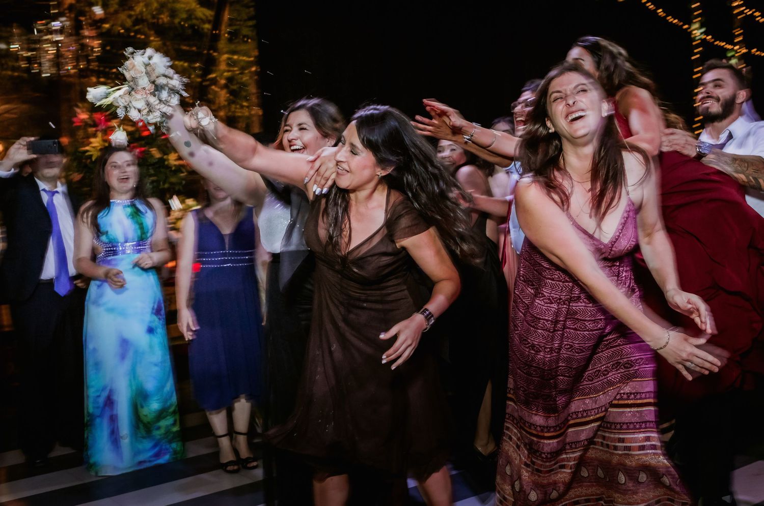 Excited wedding guests reach and compete to catch the bridal bouquet toss.