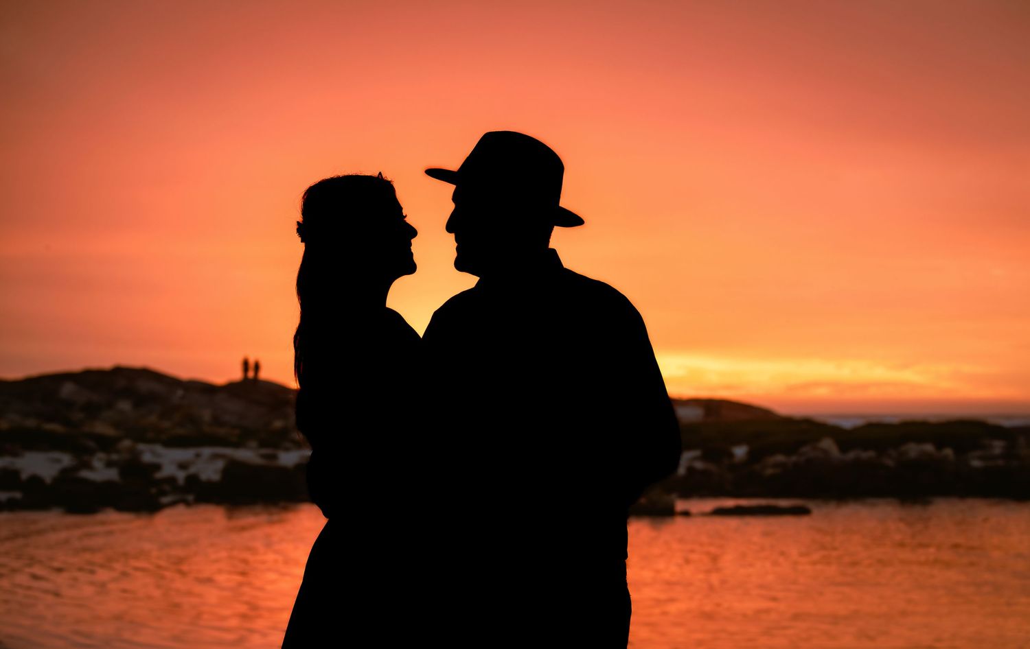 Romantic couple silhouette facing each other against glowing orange sunset backdrop.