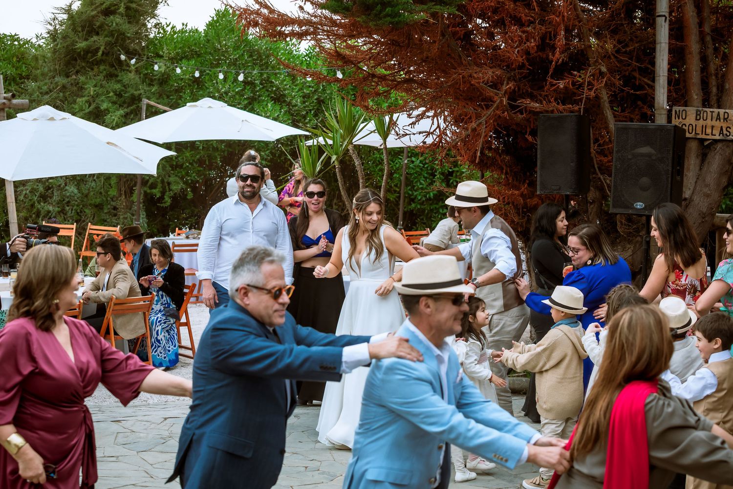 Wedding guests forming a dance line at an outdoor reception with bride in white dress.