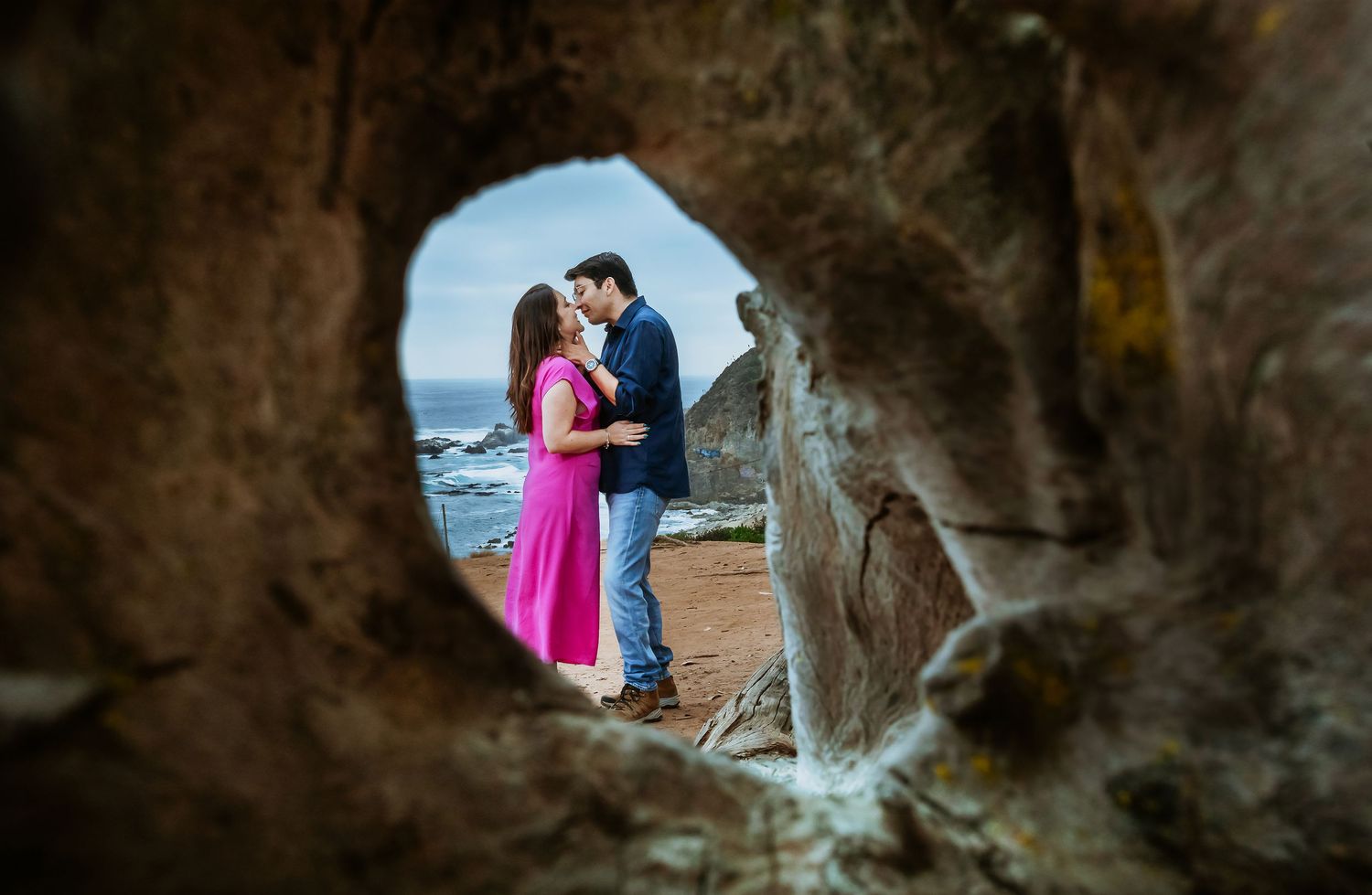 Couple sharing a romantic moment framed through a rock hole at a scenic coastal beach location.