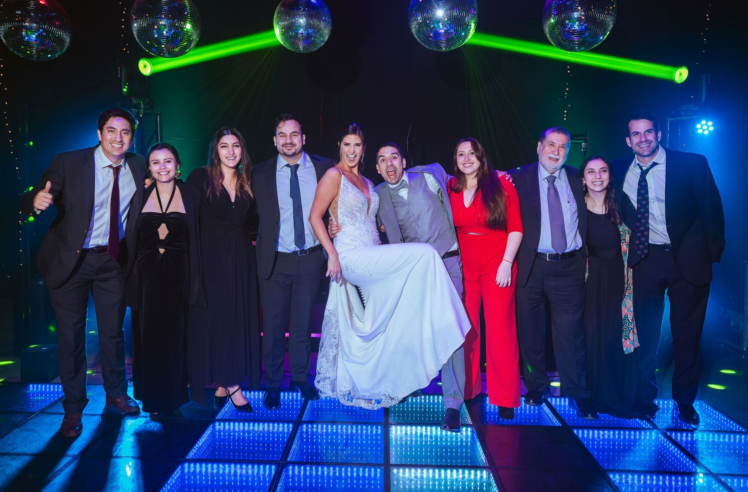 Wedding party group photo on illuminated dance floor with disco ball lights in a nightclub venue.